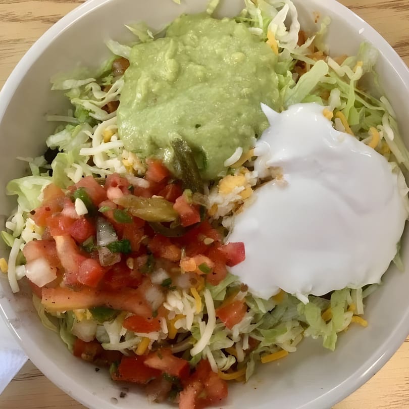 A close-up of a Mexican taco salad bowl with lettuce, pico de gallo, guacamole, and sour cream.