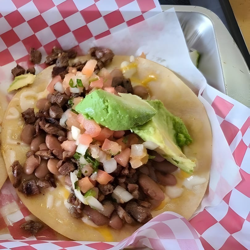 El Faro Mexican Foods taco with beans, meat, pico de gallo, and avocado slices in a red and white checkered basket.