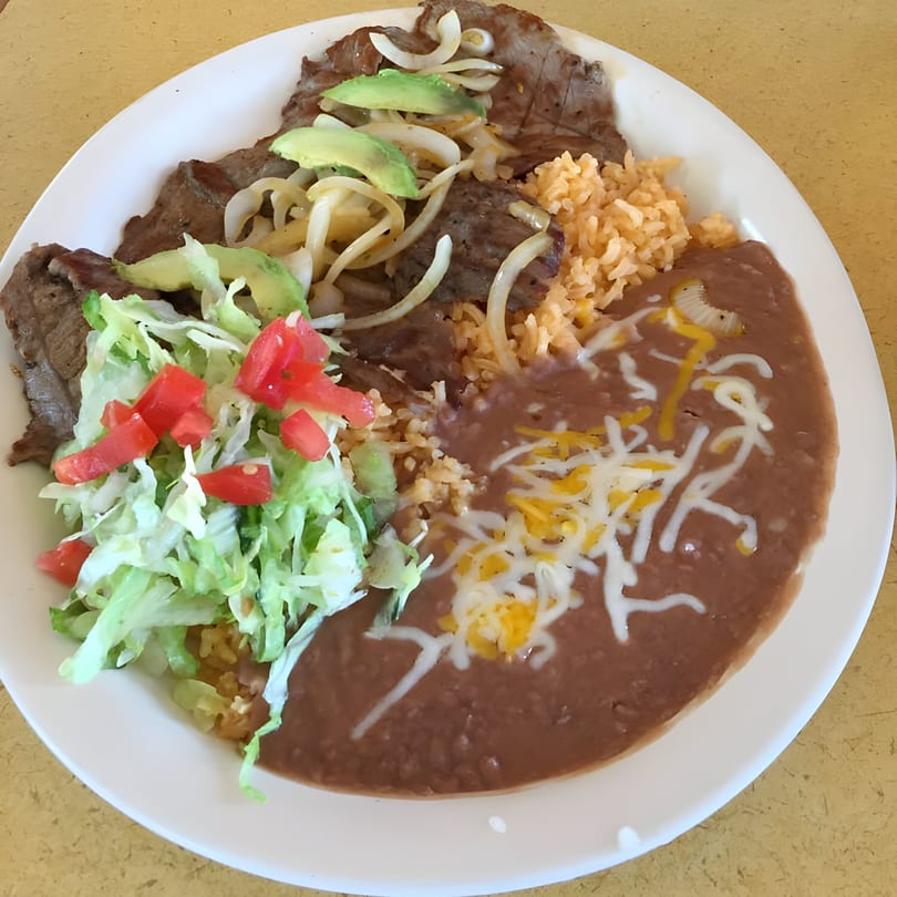 El Faro Mexican Foods' carne asada plate with rice, refried beans, avocado, onions, lettuce, and tomatoes.