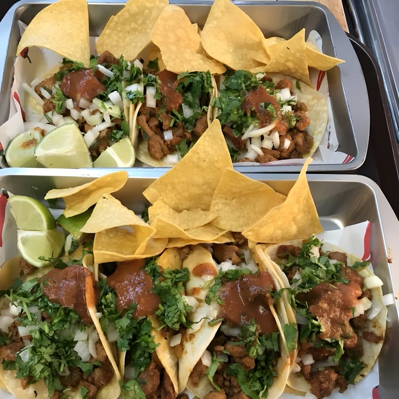 Two trays of El Faro Mexican Foods tacos with meat, cilantro, onions, salsa, lime, and tortilla chips.