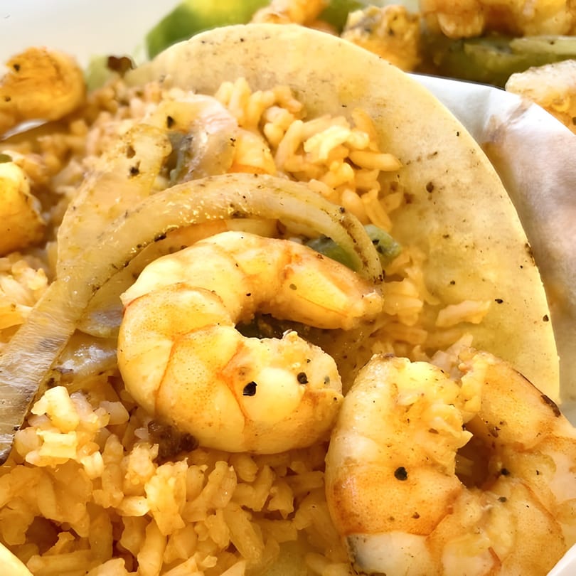 Close-up of a shrimp taco from El Faro Mexican Foods, filled with rice, onions, and seasoned shrimp.